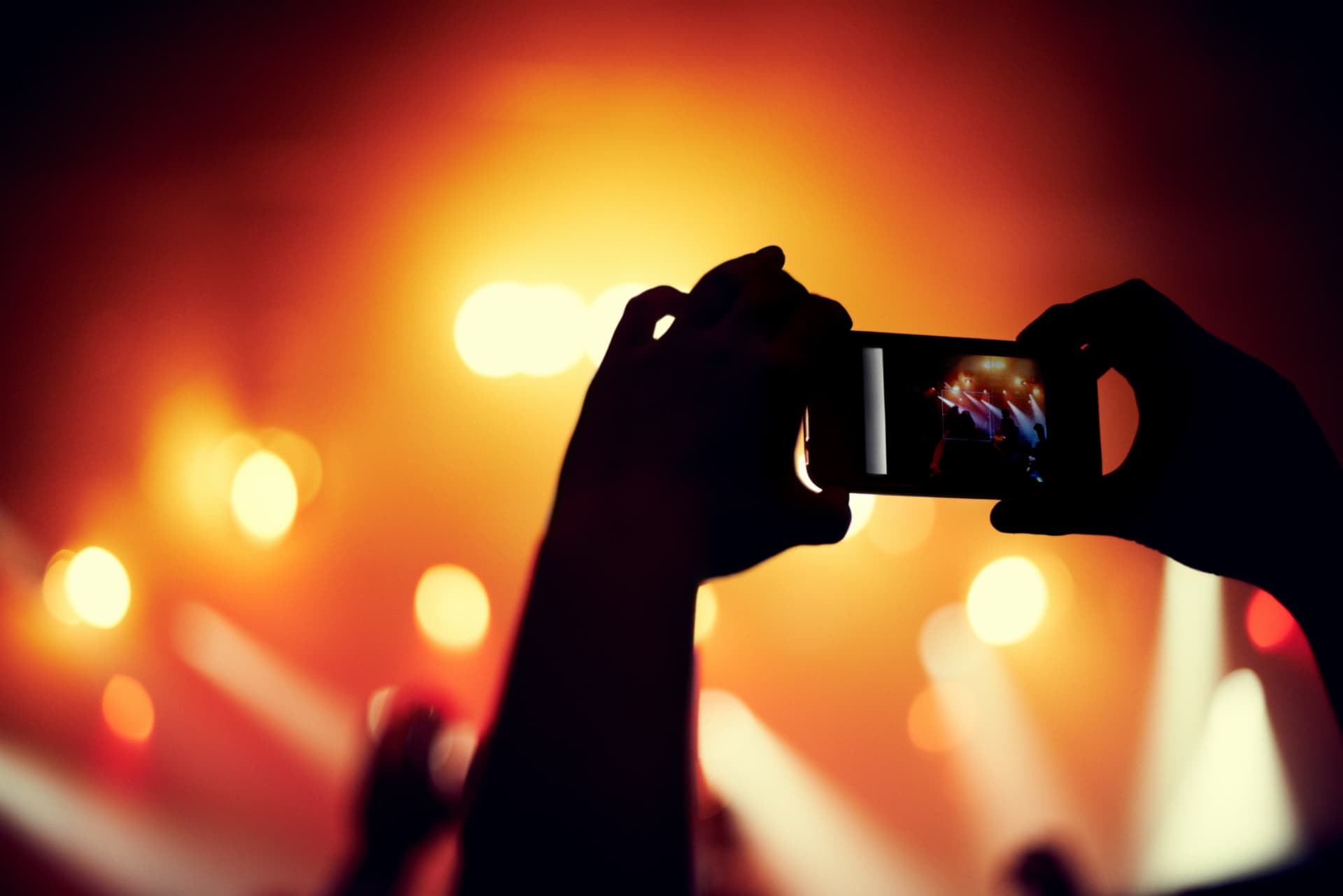 Hands holding a phone recording a live concert with warm amber lights