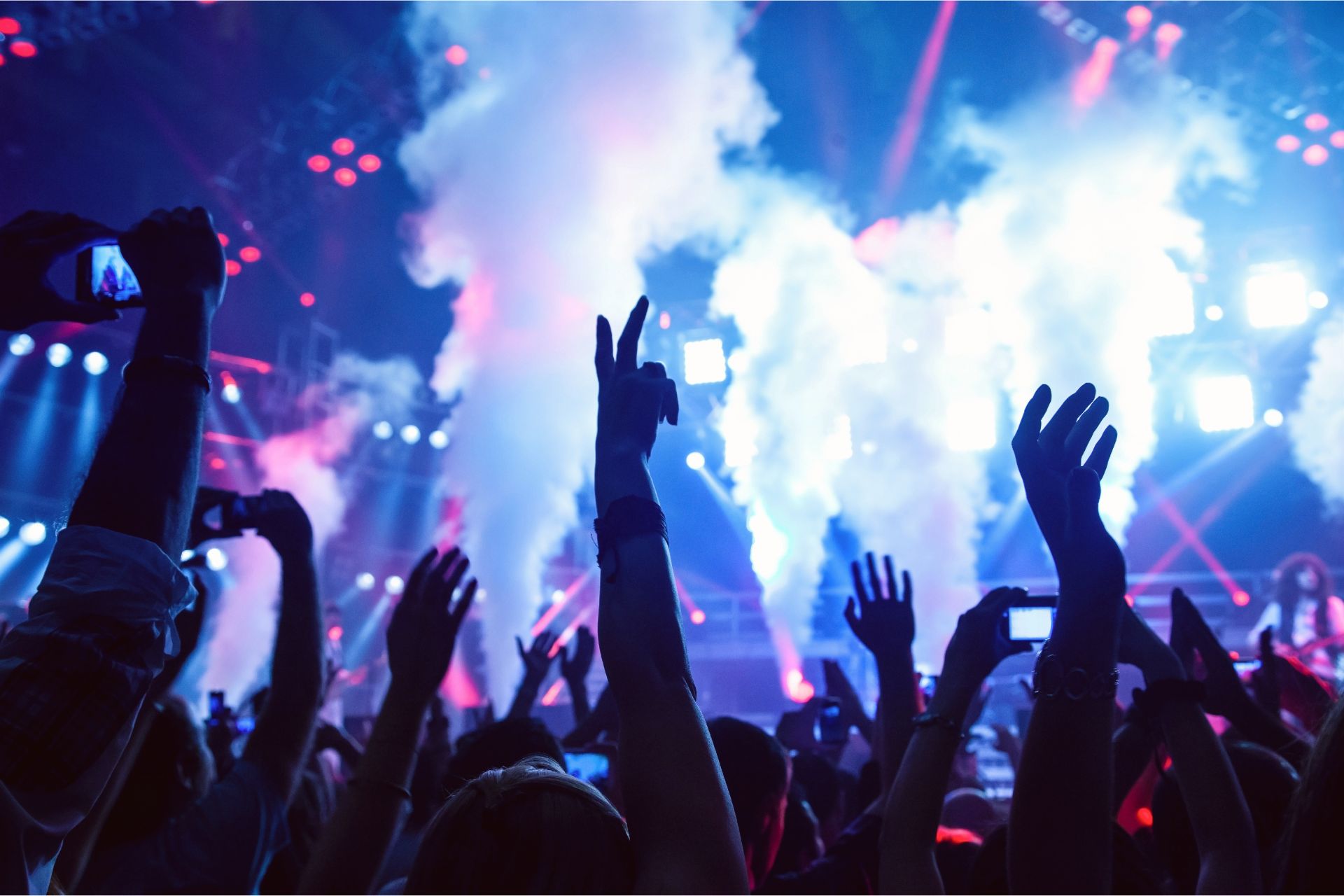 Crowd with raised hands at a live concert with blue stage lights and smoke